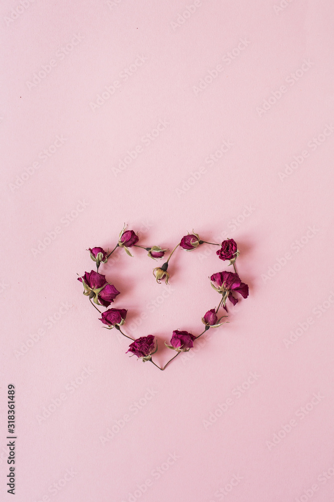 Valentine's Day concept. Heart symbol made of dried rose flower buds on pink background. Flat lay, top view minimal holiday composition.