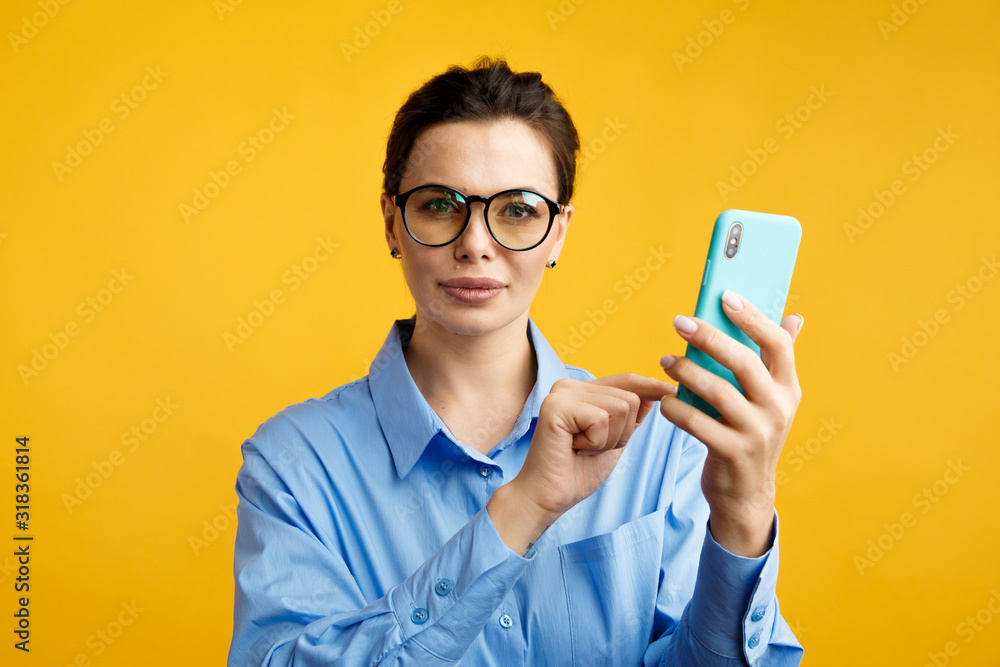 Business online. Woman in glasses using phone isolated over the yellow background