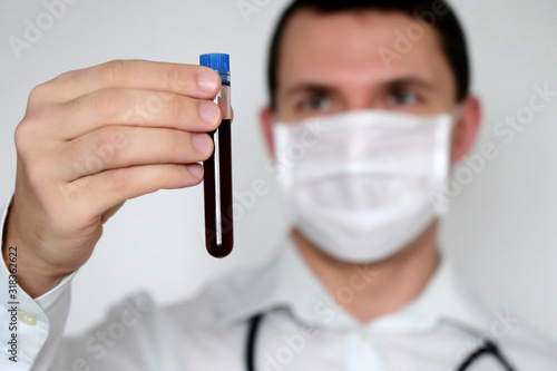 Test tube in male hand close up, doctor in medical mask holding a vial with red liquid. Concept of blood sample, vaccination, coronavirus, medical and chemical research, scientist