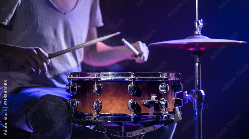 Obraz premium A drummer plays drums on a blue background. Beautiful special effects of light and smoke. The process of playing a musical instrument.