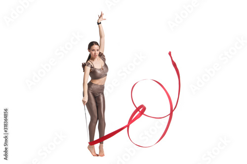 Slender graceful girl gymnast in beige sportswear dancing with a red developing ribbon isolated on a white background.