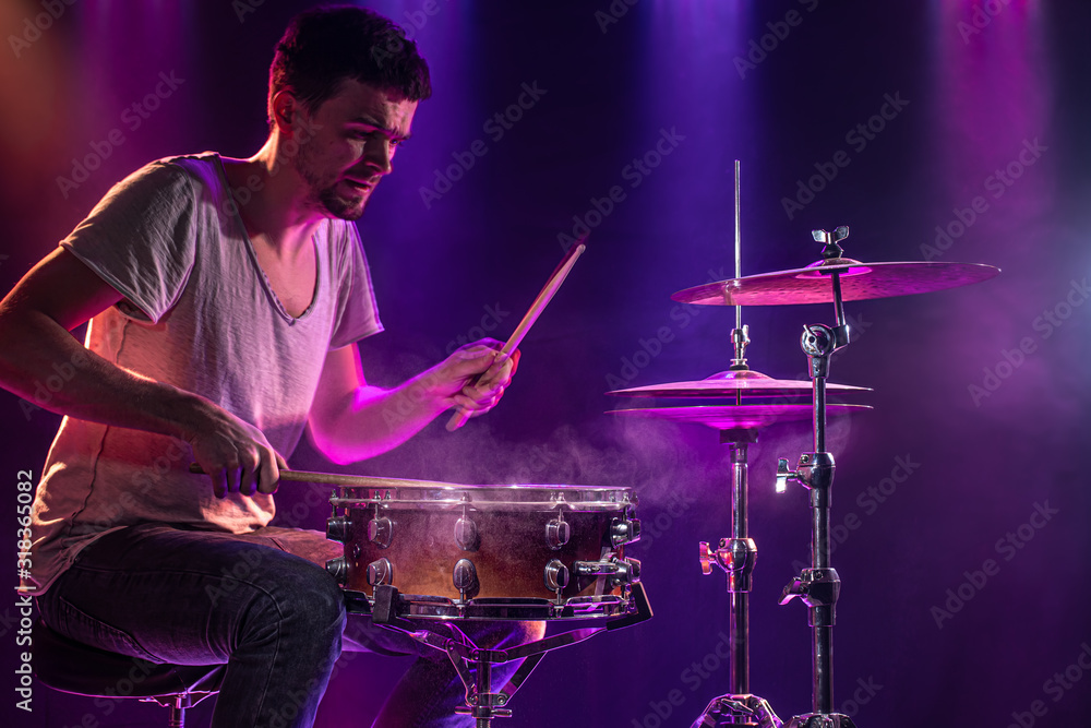 The drummer plays the drums. Beautiful blue and red background, with rays of light. Beautiful special effects smoke and lighting. The process of playing a musical instrument. Close-up photo. The drummer plays the drums. Beautiful blue and red background, with rays of light. Beautiful special effects smoke and lighting. The process of playing a musical instrument. Close-up photo.