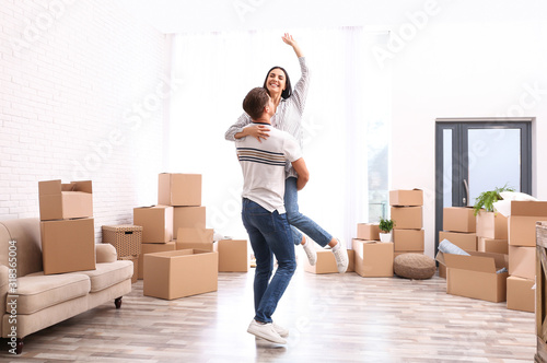 Happy couple having fun in room with cardboard boxes on moving day