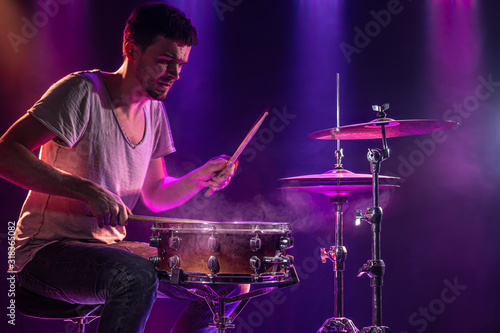 The drummer plays the drums. Beautiful blue and red background, with rays of light. Beautiful special effects smoke and lighting. The process of playing a musical instrument. Close-up photo.