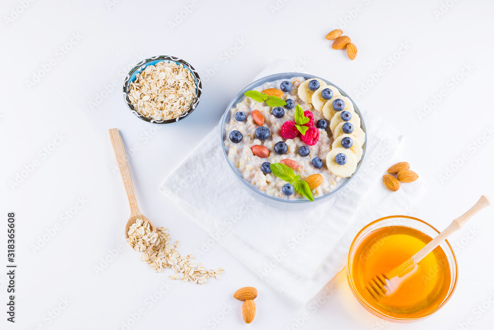 Healthy breakfast. Oatmeal with blueberries, banana and raspberry. Oatmeal with fruits and nuts in a bowl. Cooked oatmeal and honey on white background. Vegetarian food. Copy space Healthy breakfast. Oatmeal with blueberries, banana and raspberry. Oatmeal with fruits and nuts in a bowl. Cooked oatmeal and honey on white background. Vegetarian food. Copy space