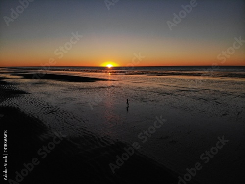 Girl in a dress standing at the beach during beautiful orange sunset on eighty mile beach  with the reflecting sun in Western Australia, Australia photo