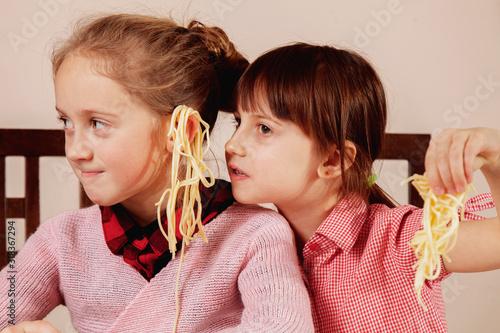 Noodles on the ears as symbol of deception and lies. Humorous portrait of two little cute child girlfriends are cheating on each other.