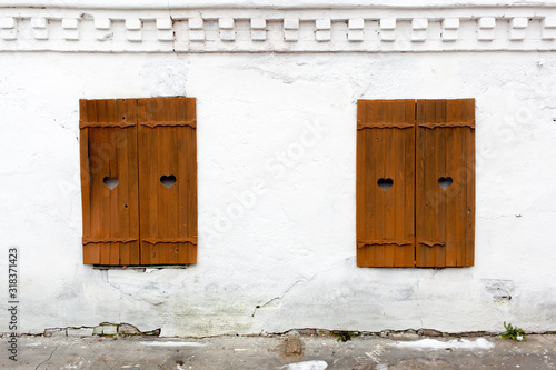 White brick wall, two windows closed with wooden shutters, old monastery