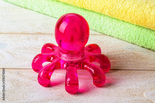 Red plastic spa massager in the form of an octopus on a white wooden surface. Massage handheld tool for limbs and body. photo