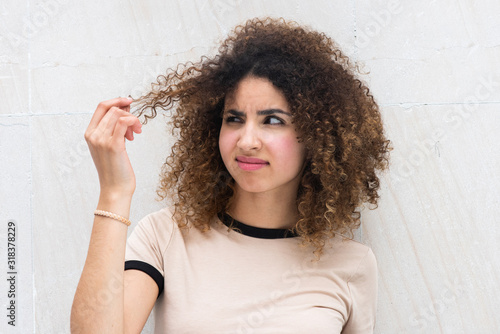 Close up young african american woman holding curly hair with unhappy expression on face