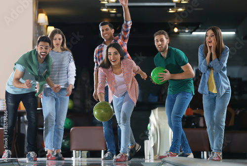 Young woman throwing ball and spending time with friends in bowling club