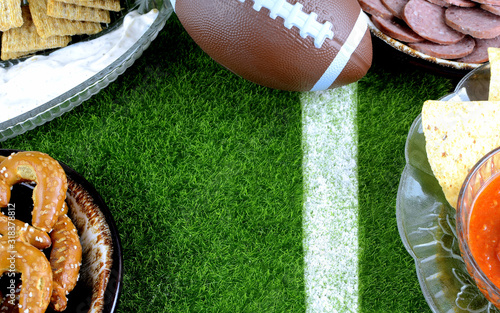 Snacks for watching a football game. Great for Super Bowl or Playoff themed projects. Pretzels, sausage, chips and dips with a football and a faux grass background