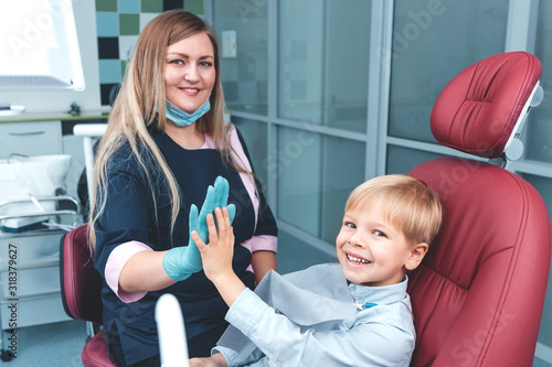 Portrait of happy female dentist and smiling young boy sitting in dental chair giving high five after teeth examination in dentistry office, healthy teeth concept