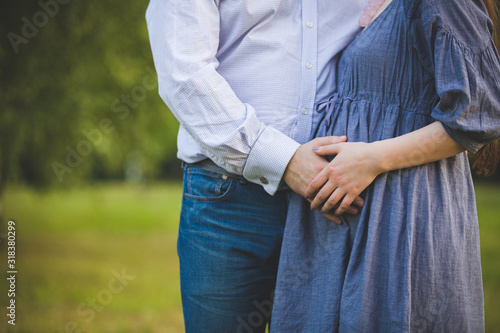 A man hugs his beloved wife and her pregnant belly. Woman waiting for the baby. A young couple walks in the park on a warm sunny day. Toning