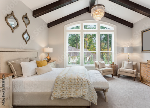 Beautiful furnished master bedroom interior in luxury home . Features vaulted ceiling with wood beams and chandelier.