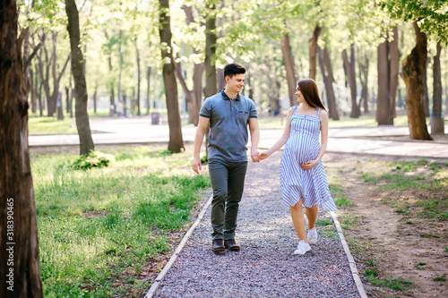 Young expectant mother and her boyfriend are walking in the park, husband and wife are walking in the fresh air waiting for the child