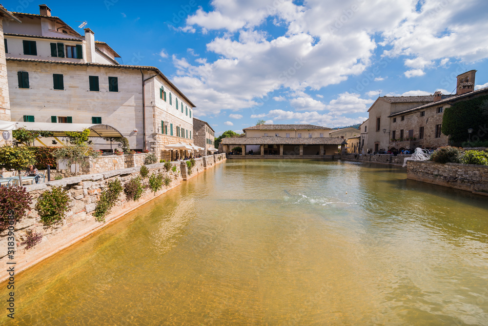 bagno vignoni natural thermal pool in a spring day with warm light sky with clouds in tuscany in italy typical small town historical village with white metal women sculptures