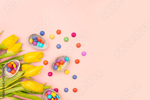 Easter border composition with chocolate eggs with colorful candies bonbons, yellow tulips on pink background. Stylish decor minimal concept. Copy space. Festive flat lay greeting card