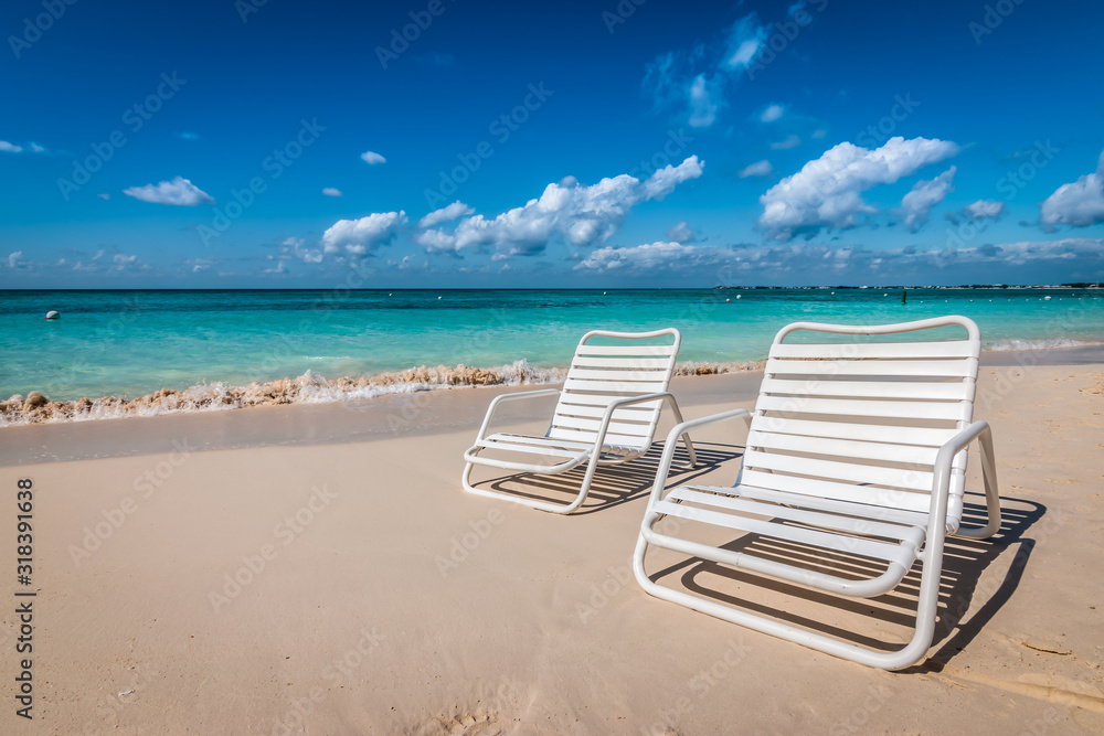 Two white beach chairs on Seven Mile Beach in Grand Cayman, Cayman Islands.