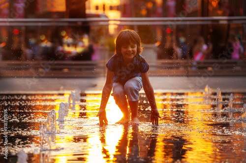 Foto Child play with street fountain touching water on Philadelphia square over sunse