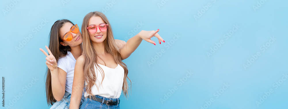 two young hipster woman friends in retro neon sunglasses standing and smiling over blue wall - obrazy, fototapety, plakaty 