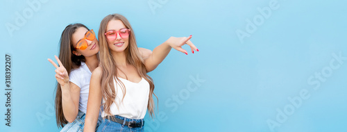 two young hipster woman friends in retro neon sunglasses standing and smiling over blue wall