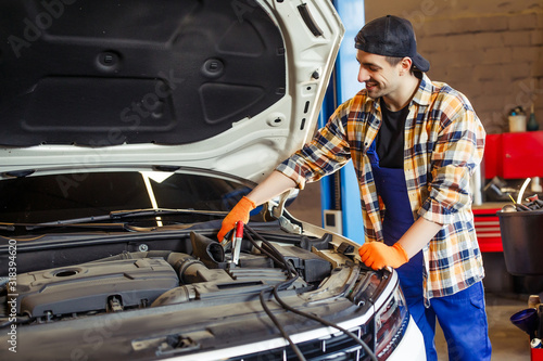 auto technician in uniform and cap charging the battery using wire cables in workshop © Тарас Нагирняк