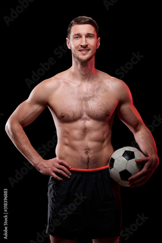 Happy muscular shirtless footballer with ball standing in front of camera
