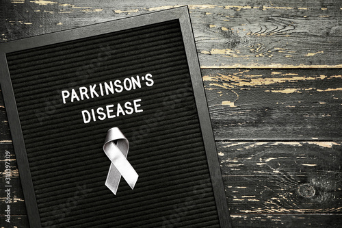 Board with text PARKINSON'S DISEASE and awareness ribbon on dark background