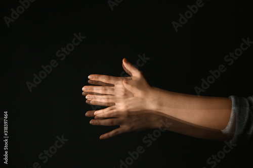 Hands of woman suffering from Parkinson syndrome on dark background
