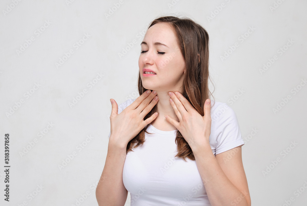 Charming girl in a white T-shirt on a gray background touches a throat that hurts a lot. Anguine disease. Charming girl in a white T-shirt on a gray background touches a throat that hurts a lot. Anguine disease.