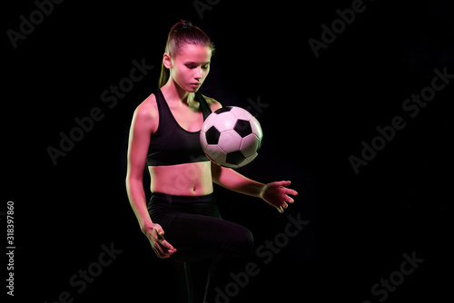 Pretty young female football player in sportswear training with soccer ball