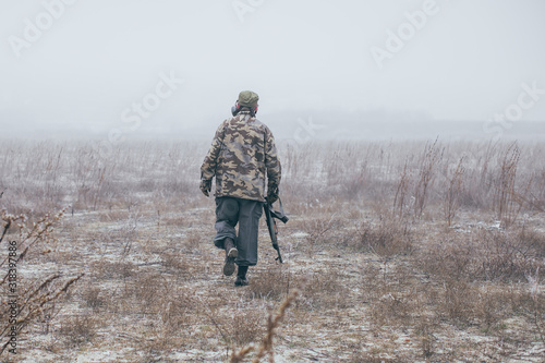 soldier with weapon walking away in field photo