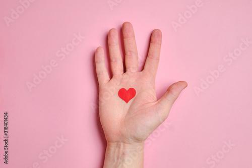 In the palm of the hand is a small red heart on a background of pink paper.
