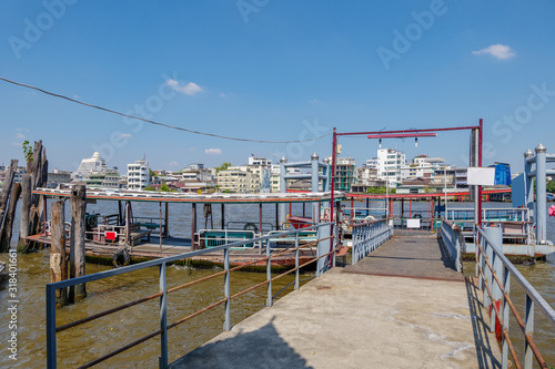 Outdoor sunny view of floating steel pontoon, pier or dock without people and small pontoon crossing river boat anchor beside pier, on Chao Phraya River, in Bangkok, Thailand.