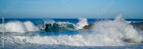 Canvas Print Large ocean waves crash against coastal stones on sunny day on European coast