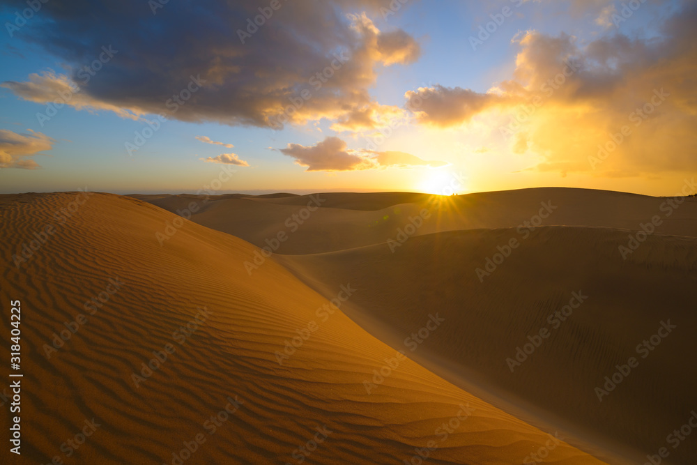 Sunset in the desert, sun and sun rays, blue sky and Beautiful clouds. Golden sand dunes in desert in Maspalomas, Gran Canaria at Canary islands, Spain