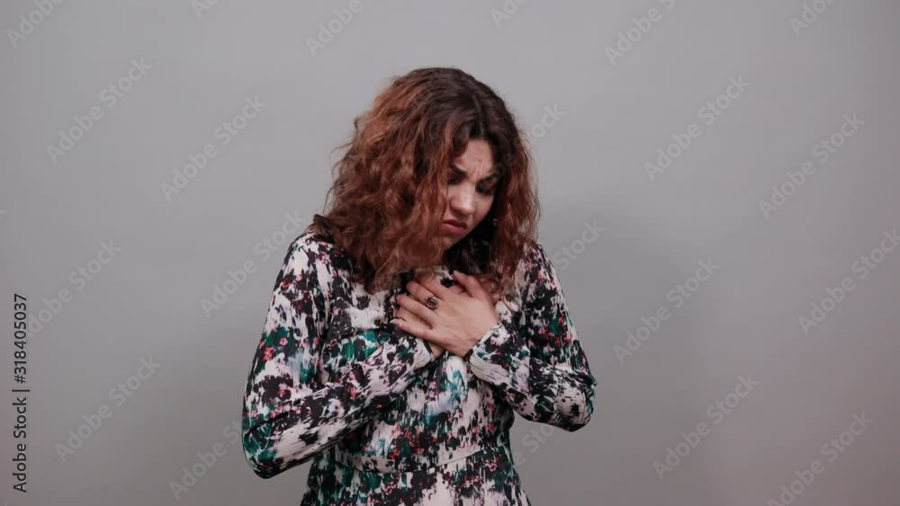 Sickness brunette caucasian young woman over isolated gray background in fashion shirt keeping hands on chest, looking disappointed. Lifestyle concept Sickness brunette caucasian young woman over isolated gray background in fashion shirt keeping hands on chest, looking disappointed. Lifestyle concept