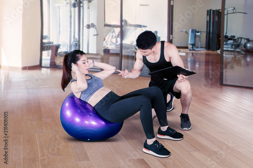 Male trainer counting asian woman doing workout