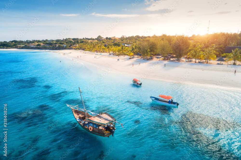 Aerial view of the fishing boats on tropical sea coast with sandy beach at sunset. Summer holiday in Zanzibar, Africa. Landscape with boat, yacht in transparent blue water, green palm trees. Top view - obrazy, fototapety, plakaty 