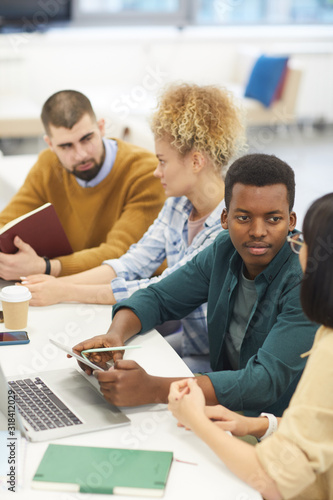 High angle view at multi-ethnic group of students studying in college library  focus on African-American man talking to partner