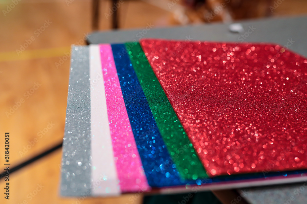 Obraz premium Upclose photo of a pile of colorful rectangular paper tiles covered with sparkling glitter laying in stack on a table