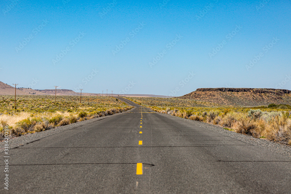 Old straight asphalt road with yellow dashed line leading into the horizon in the middle of nowhere, south Oregon.