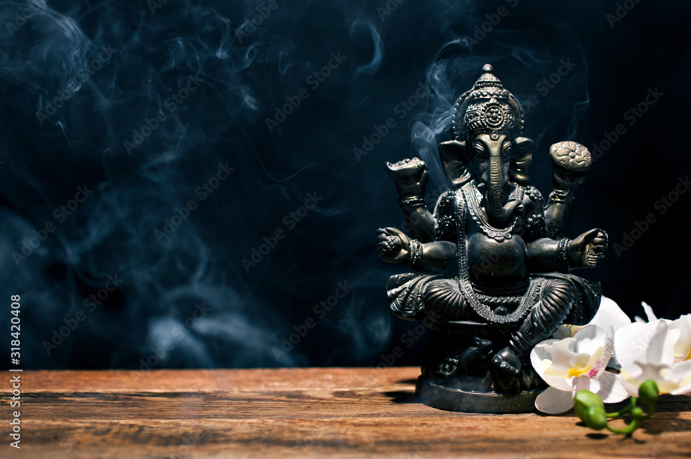 Hindu god Ganesh on black background. Statue on wooden table with a smoke of incense. Copy space. - obrazy, fototapety, plakaty 