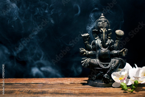 Hindu god Ganesh on black background. Statue on wooden table with a smoke of incense. Copy space. photo