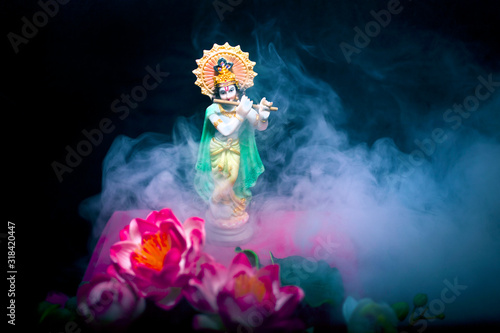 Hindu god Krishna. Statue with a smoke and lotus flowers on a black background