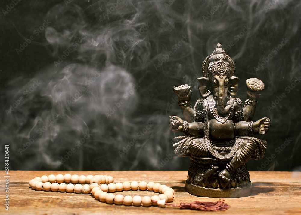 Hindu god Ganesh on black background. Statue and rosary on wooden table  with a smoke of incense. Copy space. Stock Photo | Adobe Stock