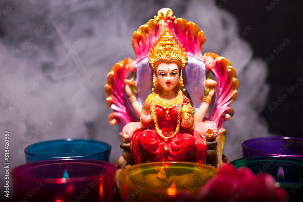 Hindu goddess Lakshmi. Statue with a smoke, candles and lotus flowers on a black background