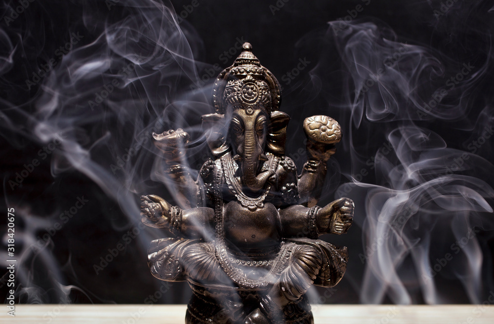 Hindu god Ganesha on black background. Statue on wooden table with a smoke  of incense. Stock Photo | Adobe Stock