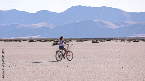 A teen age girl riding a bike on a playa of Alvord lake against Steens mountains in the background